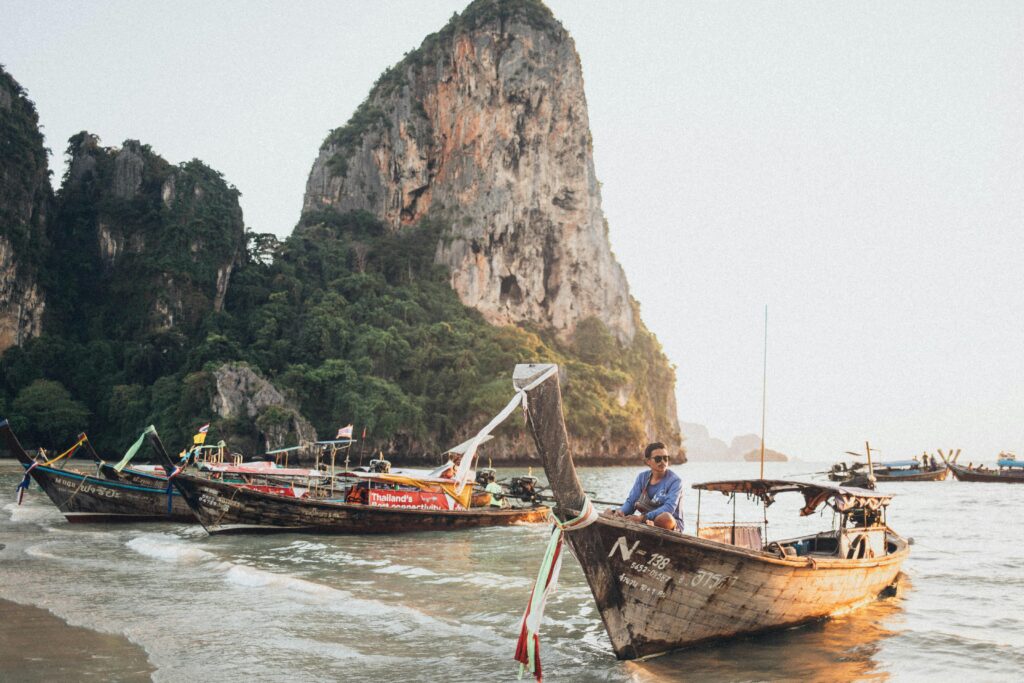 A serene beach scene with traditional long-tail boats and majestic cliffs in Thailand, showcasing coastal life.